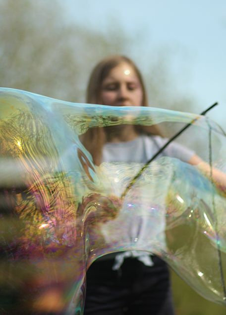 Mädchen macht draußen in der Natur große Seifenblasen