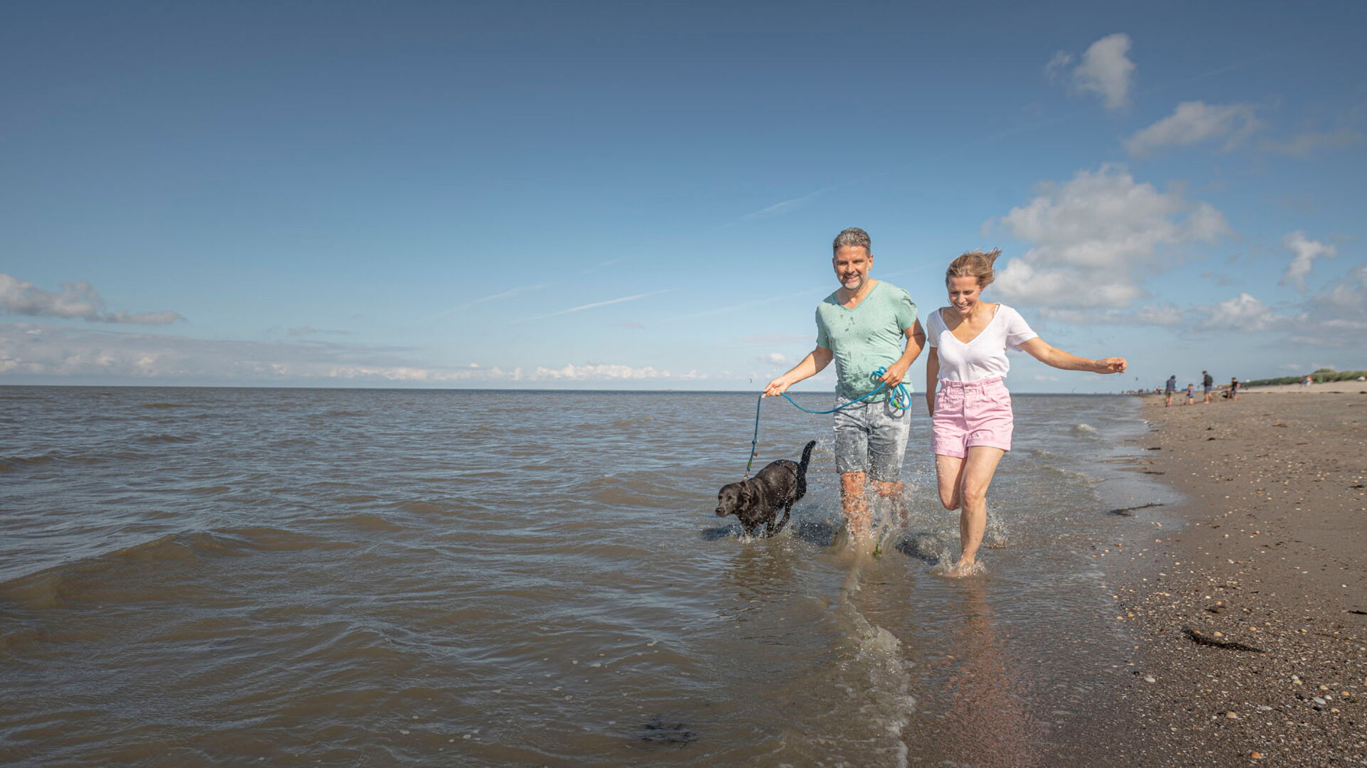 Mann und Frau laufen mit Hund am Strand entlang